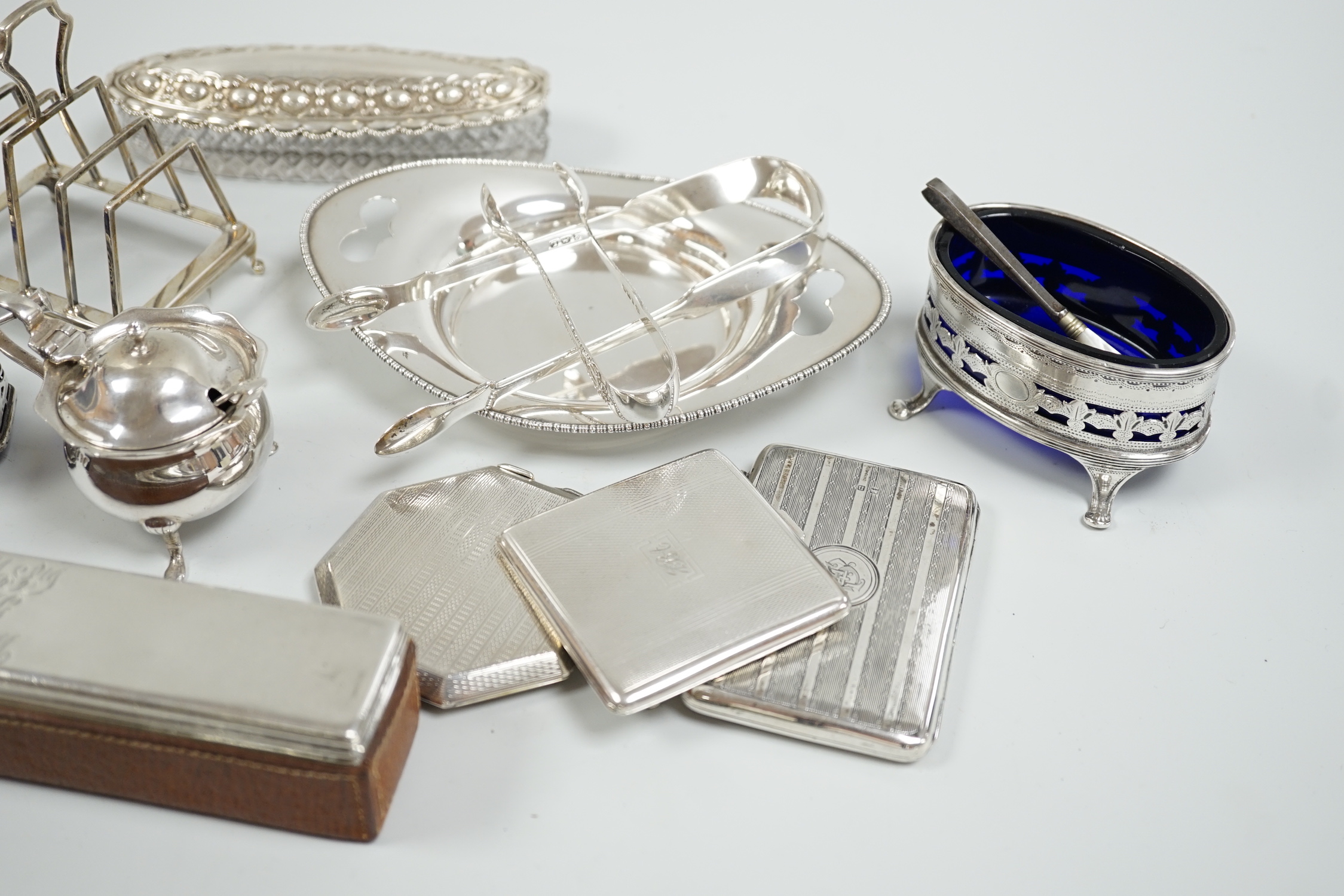 A group of mixed silver ware including a manicure stand, toastrack, purse, two compacts, four condiments, two pairs of sugar tongs, a stand and two mounted glass toilet jars.